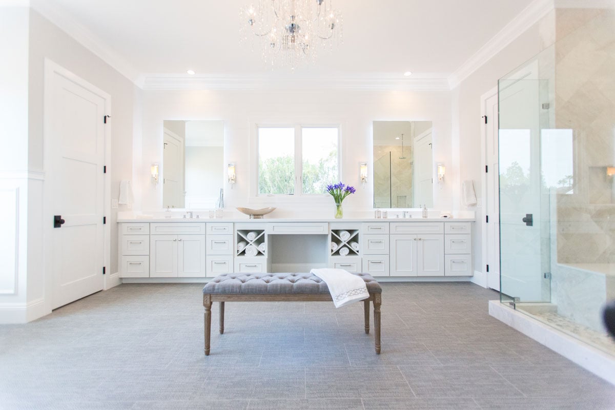 Full room view of all white bathroom with a chandelier over the bench